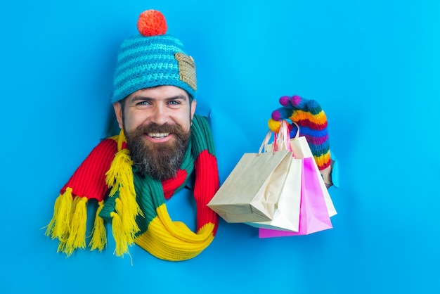Un bel homme barbu tient un paquet de magasins à la main à travers un trou de papier barbu en couleurs chaudes