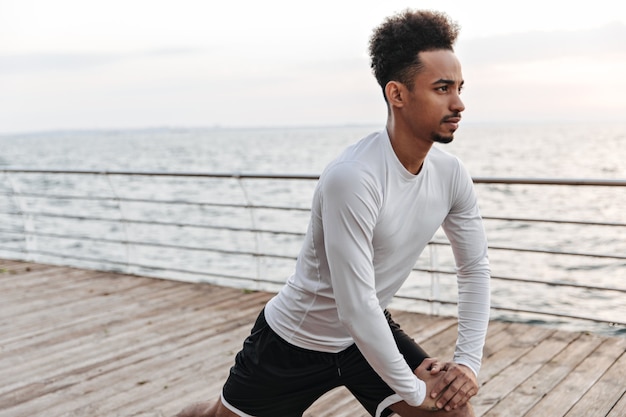 Photo gratuite bel homme brune frisée en short noir et t-shirt à manches longues s'étend à l'extérieur