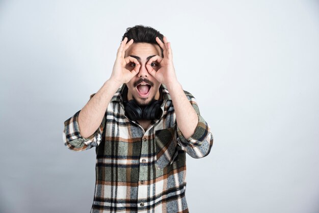 bel homme avec un casque faisant des yeux binoculaires sur un mur blanc.