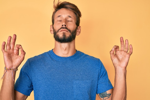 Bel homme caucasien avec barbe portant des vêtements décontractés se détendre et souriant avec les yeux fermés faisant un geste de méditation avec les doigts concept de yoga