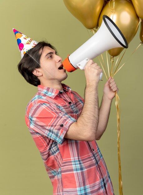 Un Bel Homme Caucasien Confiant Portant Une Casquette D'anniversaire Se Tient Sur Le Côté Tenant Des Ballons à L'hélium Et Parle Dans Un Haut-parleur