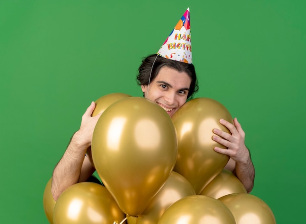 Un bel homme caucasien souriant portant une casquette d'anniversaire tient des ballons à l'hélium