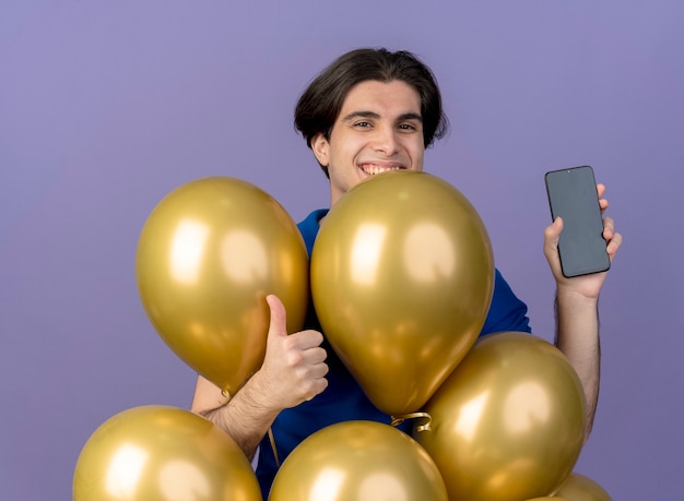 Photo gratuite un bel homme caucasien souriant se tient debout avec des ballons à l'hélium et tient le téléphone