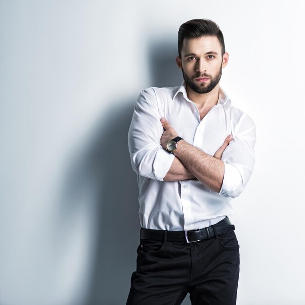 Bel homme en chemise blanche et pantalon noir - posant un mec attrayant avec une coiffure de mode. Homme confiant avec une barbe courte. Garçon élégant adulte aux cheveux bruns.