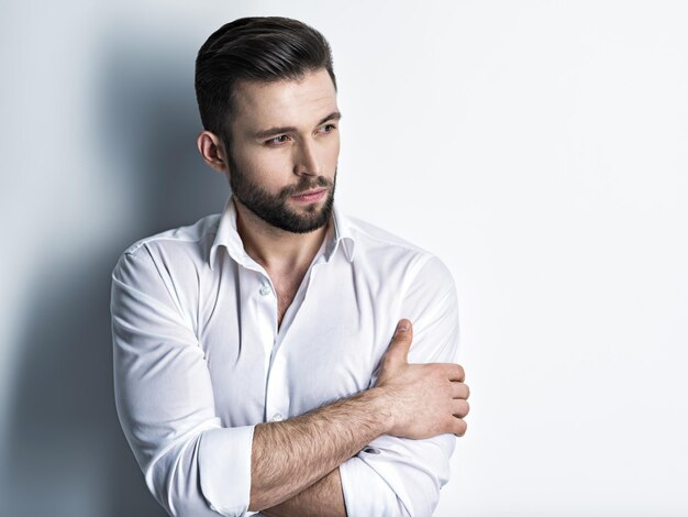 Bel homme en chemise blanche, posant. Mec attrayant avec une coiffure de mode. Homme confiant avec une barbe courte. Garçon adulte aux cheveux bruns. Portrait en gros plan.