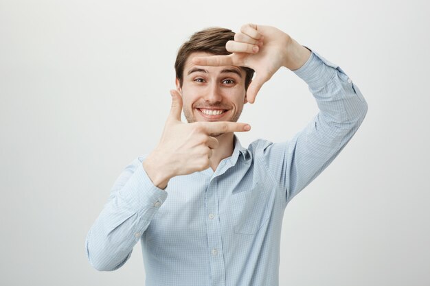 Bel homme créatif souriant, montrant les cadres de la main, capturez le moment