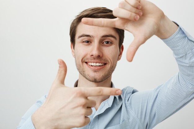 Bel homme créatif souriant, montrant les cadres de la main, capturez le moment