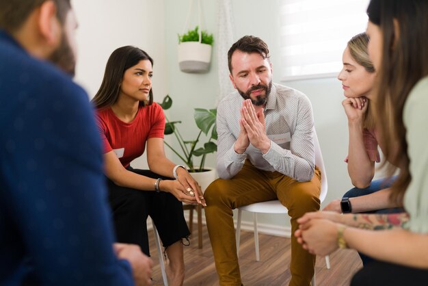 Bel homme dans la trentaine partageant son expérience de la dépendance à l'alcool dans un groupe AA. Jeunes en thérapie de groupe écoutant les problèmes d'un membre latin