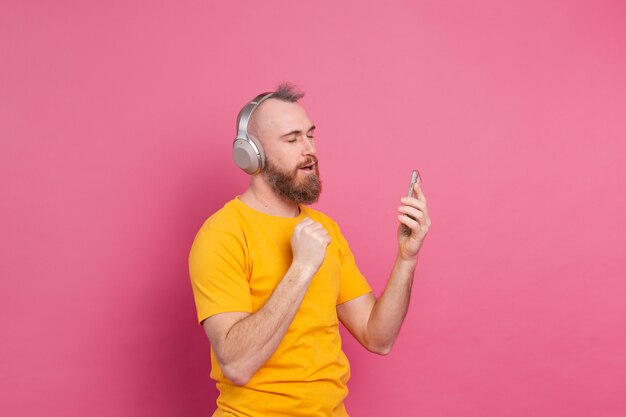 Bel homme en danse décontractée avec téléphone portable et casque isolé sur fond rose