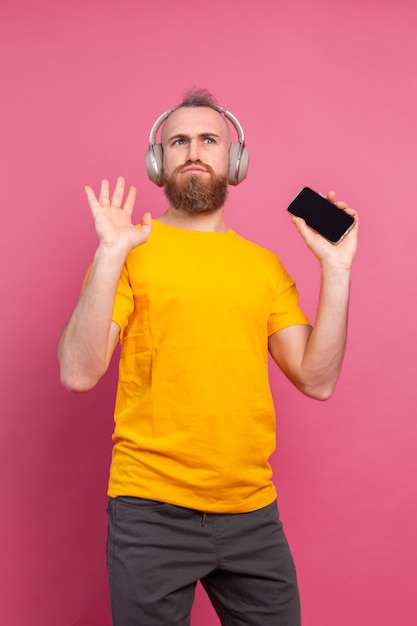 Bel homme en danse décontractée avec téléphone portable et casque isolé sur fond rose