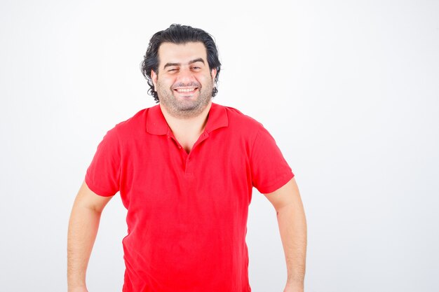 Bel homme debout droit, souriant en t-shirt rouge et à la gaieté. vue de face.