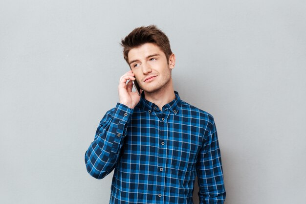 Bel homme debout sur un mur gris et parler par téléphone.