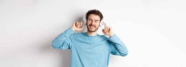 Bel homme écoutant de la musique dans des écouteurs sans fil et souriant en profitant d'un bon son sur fond blanc