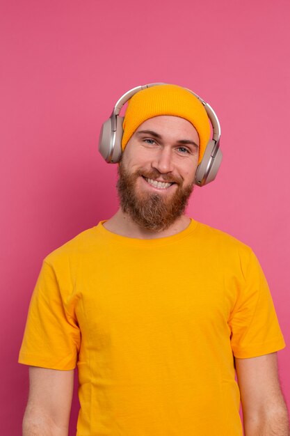 Bel homme en écoute décontractée de la musique avec un casque isolé sur fond rose