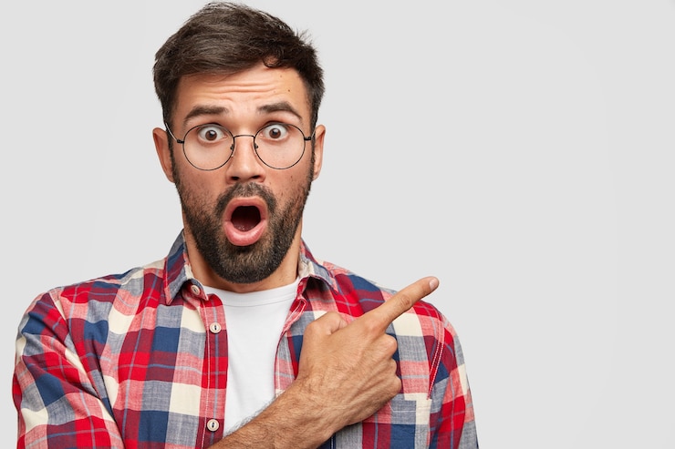 Photo gratuit un bel homme effrayé avec une expression étonnée montre un espace vide, dit regarder là-bas, exprime une attitude négative