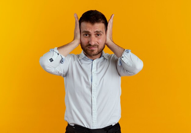 Bel homme ennuyé ferme les oreilles isolés sur un mur orange