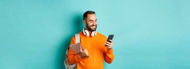 Photo gratuite bel homme étudiant avec casque et sac à dos tenant un message de lecture de tablette numérique sur mobile p