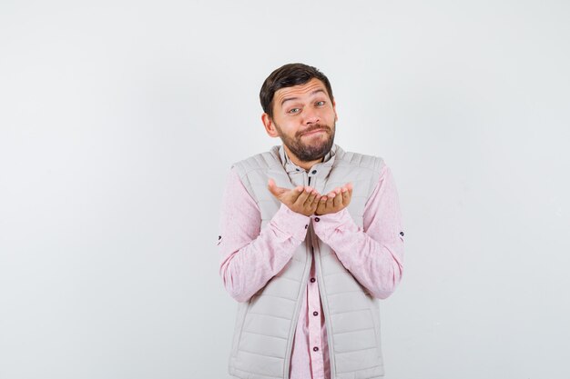 Bel homme faisant le geste de donner en gilet, chemise et semblant sincère,