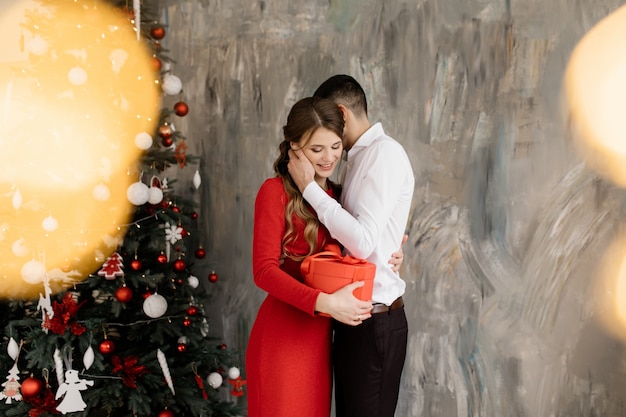 Bel homme et femme dans fantaisie ferme pose avant riche décoré arbre de noël et échange leur