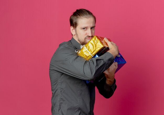 Bel homme gourmand se tient sur le côté tenant des coffrets cadeaux à isolé sur mur rose