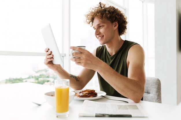 Photo gratuite bel homme heureux à l'aide de la tablette tactile et de boire du café