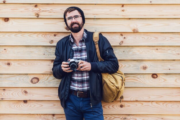 Bel homme hipster avec barbe, chapeau élégant et lunettes posant avec appareil photo rétro en mains