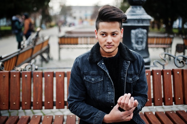 Photo gratuite bel homme indien à la mode en veste de jeans noir posé en plein air assis sur un banc