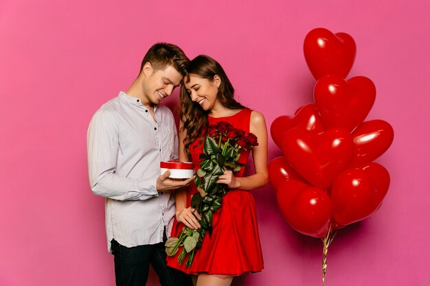 Bel homme et jolie femme regardant boîte avec cadeau, roses rouges