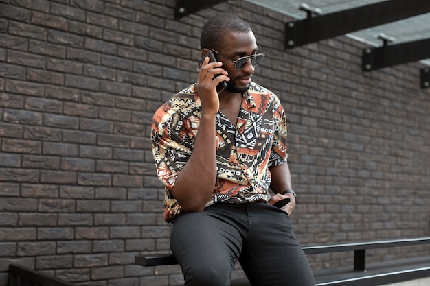 Bel homme avec des lunettes de soleil à l'aide d'un smartphone moderne à l'extérieur