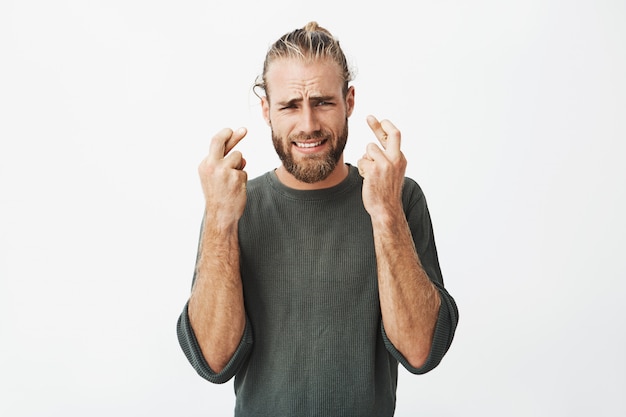 Bel homme mal rasé tenant les doigts croisés avec une expression inquiète