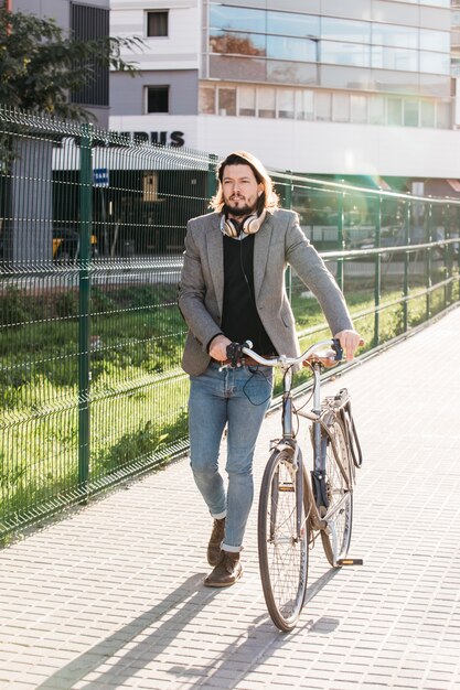 Un bel homme marchant à vélo devant le bâtiment