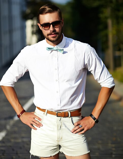 Bel homme modèle hipster dans des vêtements d'été élégants posant dans des lunettes de soleil