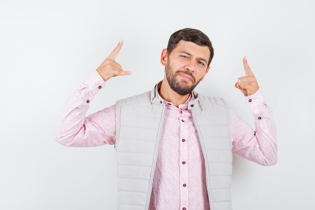 Bel homme montrant un geste rock en gilet, chemise et l'air confiant.