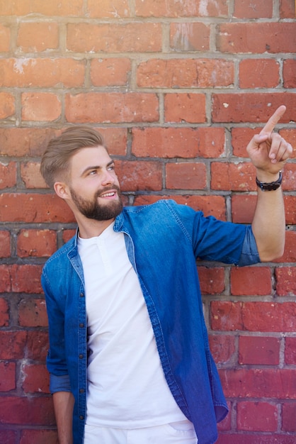 Photo gratuite bel homme montrant sur le mur de briques