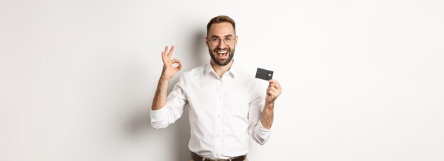 Bel Homme Montrant Sa Carte De Crédit Et Bon Signe Recommandant La Banque Debout Sur Fond Blanc