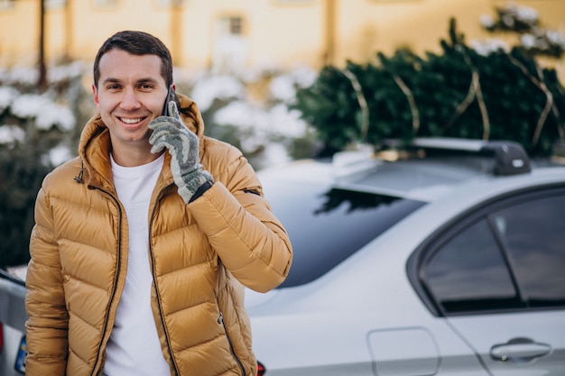 Bel homme parlant au téléphone par la voiture avec arbre de Noël sur le dessus