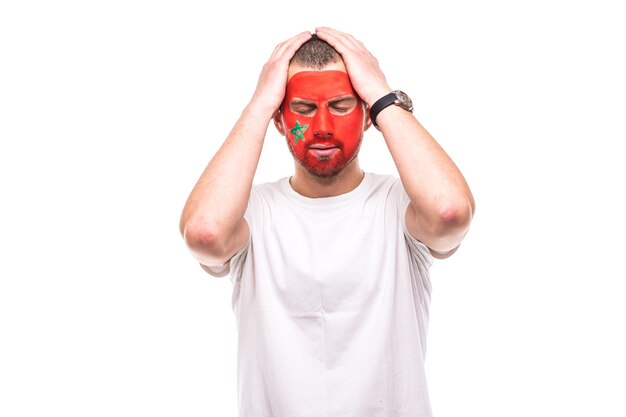 Bel homme partisan fan de l'équipe nationale du Maroc peint le visage du drapeau obtenir des émoitions tristes et frustrés dans une caméra. Émotions des fans.