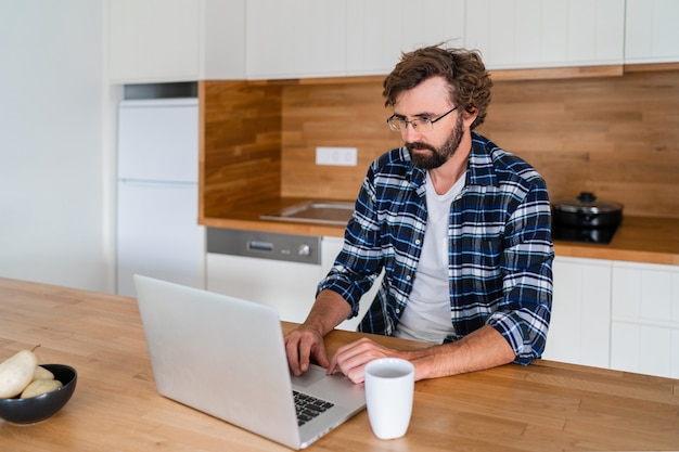 Bel homme pigiste utilisant un ordinateur portable étudiant le travail en ligne à domicile
