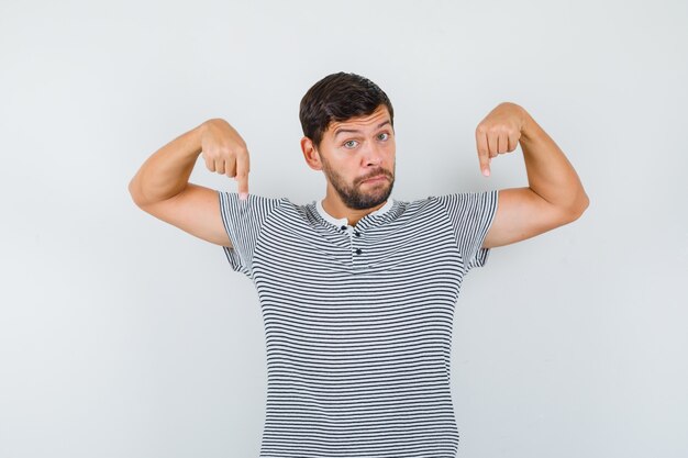 Bel homme pointant vers le bas en t-shirt et l'air surpris. vue de face.