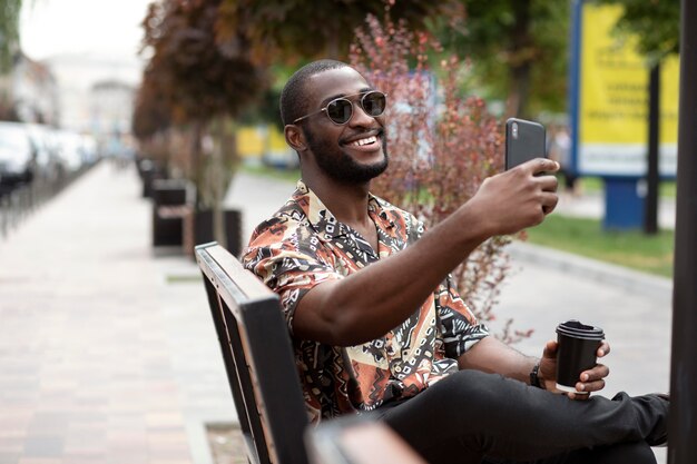 Bel homme prenant selfie avec un smartphone moderne à l'extérieur