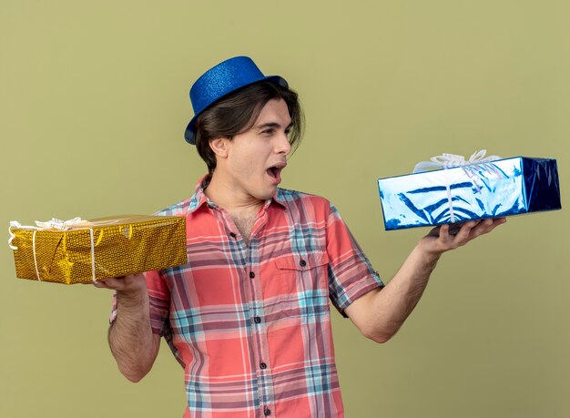 Bel homme de race blanche agacé portant un chapeau de fête bleu détient des coffrets cadeaux