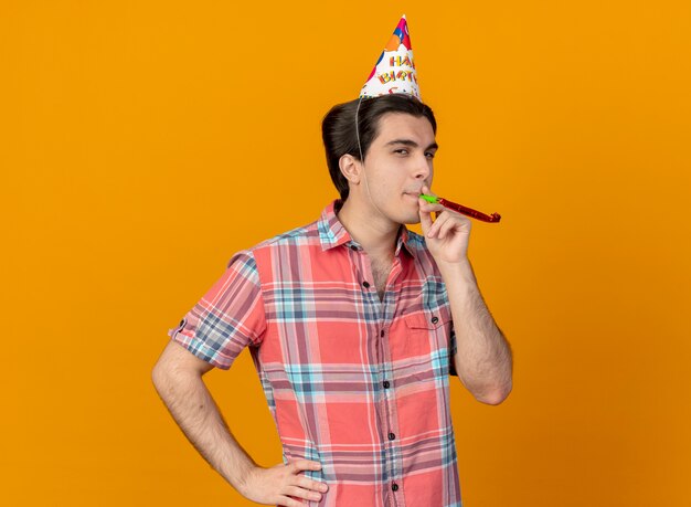 Bel homme de race blanche confiant portant une casquette d'anniversaire soufflant un sifflet de fête