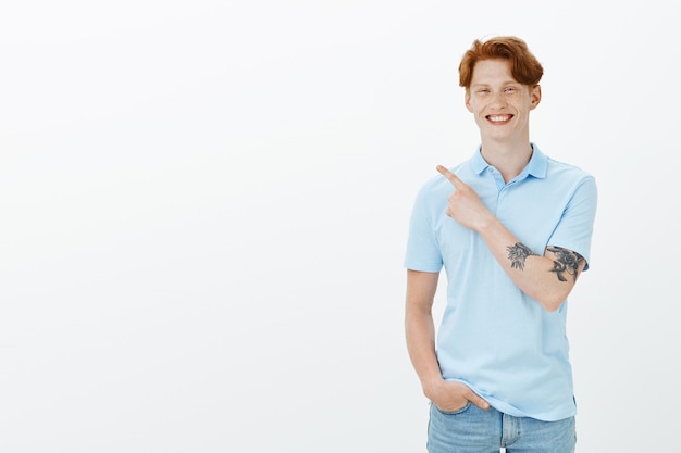 Bel homme rousse insouciant pointant le coin supérieur gauche et souriant, montrant la publicité