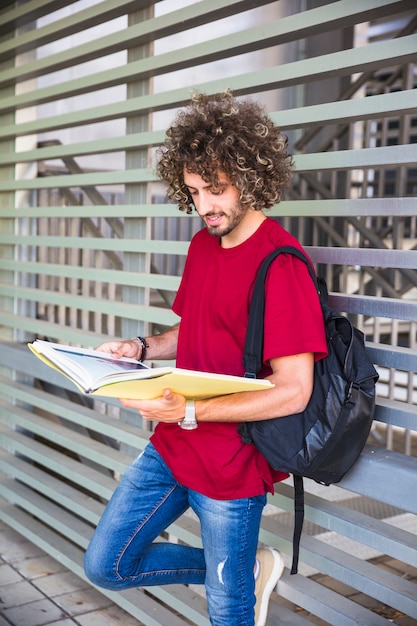 Photo gratuite bel homme avec sac à dos, livre de lecture