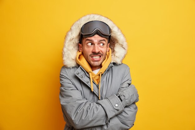 Bel homme se sent très froid dehors tremble pendant une journée glaciale se serre dans ses bras pour se réchauffer les dents vêtu d'un manteau d'hiver avec capuche.