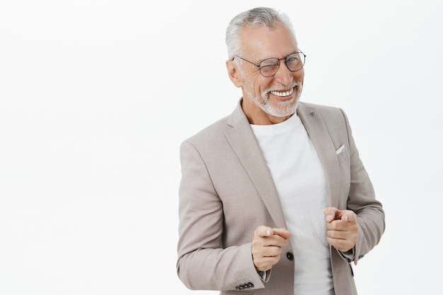 Bel homme senior réussi en costume pointant du doigt, souriant impertinent