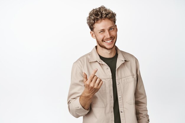 Bel homme souriant demandant à se rapprocher vous attirant l'air amical et vous invitant à l'approcher debout sur fond blanc