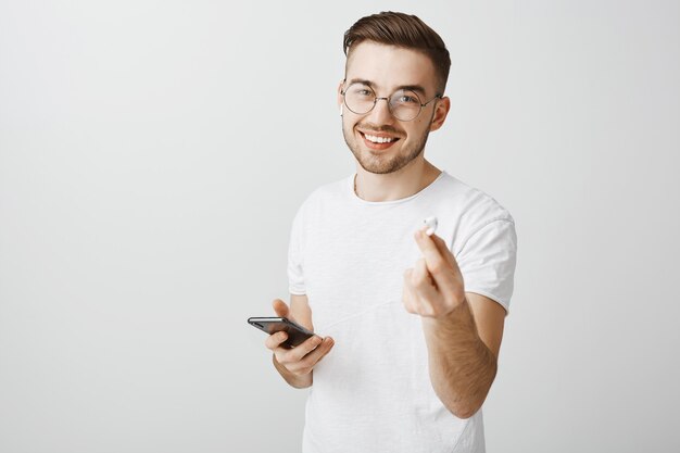 Bel homme souriant à lunettes suggère son écouteur pour écouter de la musique ensemble, vous donnant des écouteurs