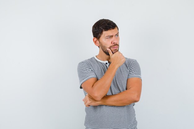 Bel homme en t-shirt debout dans une pose de réflexion et l'air pensif, vue de face.