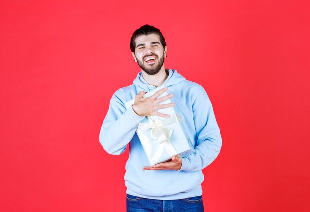 Bel homme tenant une boîte-cadeau emballée avec les deux mains sur le mur rouge